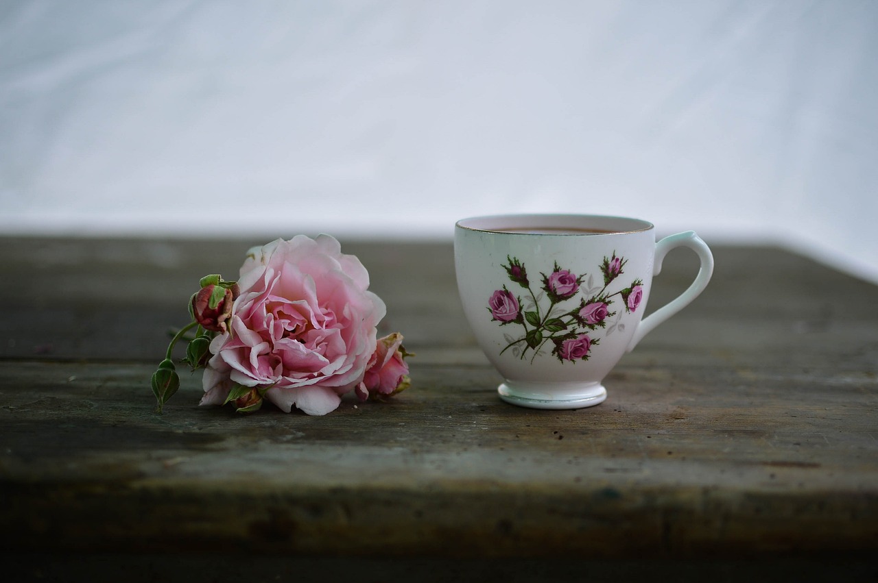 Ruusukuvioinen kahvikuppi ja sen vieressä vaaleanpunainen ruusu